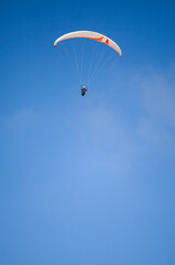 A paragliding athlete is floating in the air showing his skills in controlling a paraglider against a backdrop of bright blue sky.