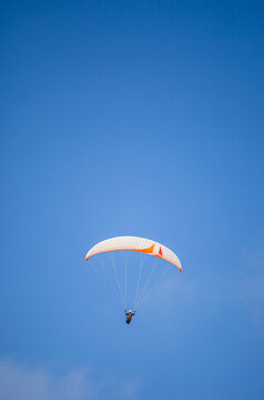A paragliding athlete is floating in the air showing his skills in controlling a paraglider against a backdrop of bright blue sky.