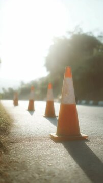 Orange traffic cones stand in a row on the road, creating safety along the route under the bright sun, vertical image, street.