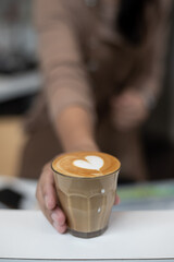 Close-up of barista hand serving latte art in a coffee cup