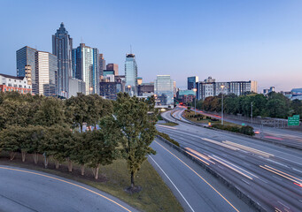 Downtown Atlanta Skyline showing several prominent buildings, highways, cars, light trails and hotels under a blue sky.