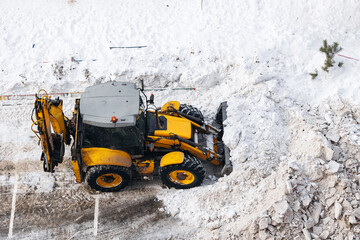 Yellow tractor clearing snow on winter road with pile of ice