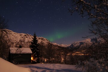 The Northern Lights Dancing Above a Snowy Cabin