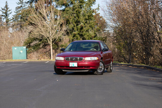 Portland, OR, USA - Dec 5, 2020 - 2003 burgundy Buick Century sedan parked on asphalt. American four-door passenger car with chrome wheels, compact body, and vintage design in suburban area