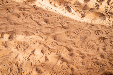 Multiple overlapping footprints and shoe treads pressed into the soft red sand of a desert trail, capturing the impact of foot traffic in a dry, sunlit landscape in the American Southwest