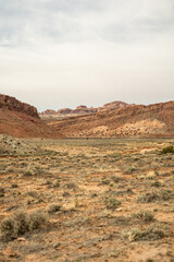 A wide desert valley in the American Southwest with sparse vegetation and dramatic red cliffs under a hazy sky