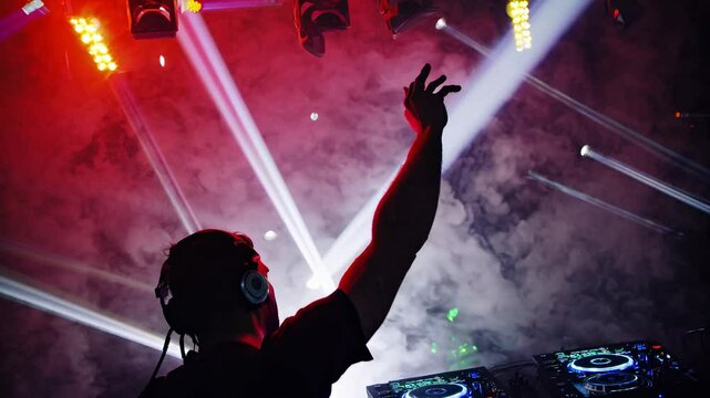 Silhouette of a DJ with headphones against a smoky backdrop, captured from a low angle. The scene evokes a dynamic, atmospheric video style.