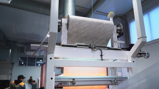 Unrolling foil sheet with marble pattern on production line in workshop. Laminating film for plastic profile decor in manufacturing facility