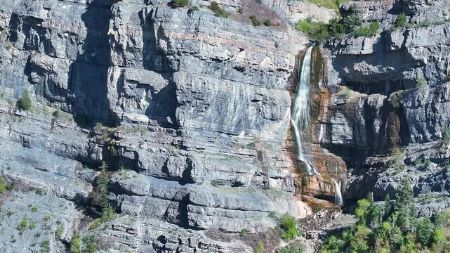 Aerial mountain Bridal Veil Falls Provo Utah 1 sliding. 607 foot tall double cataract waterfall in Provo Canyon. Rugged rocky ledges and cliffs over pine forests. Deep canyon valley. Summer.