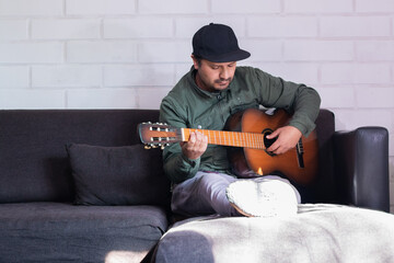 latino man sitting on sofa plays guitar with left hand
