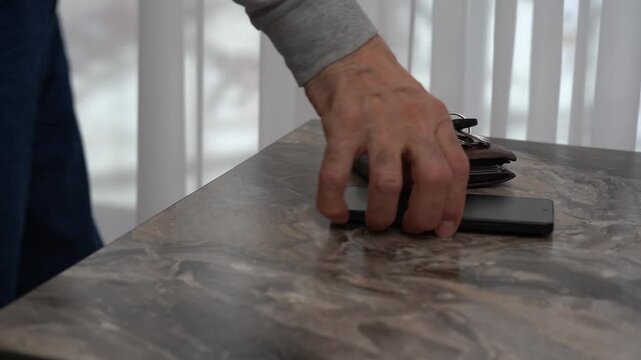 Hand reaching for smartphone and keys on table in daylight.
