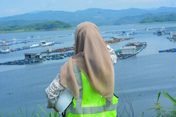A female fish farm manager wears a safety vest and carries a book to check the work.