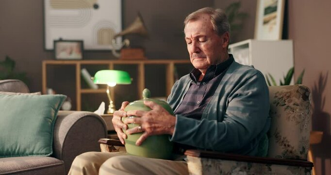 Home, death and senior man with grief, urn and thinking of loss in living room, mourning and sadness. Retirement, widower and elderly person with memories, contemplating and depression in house