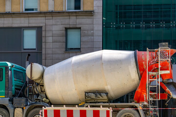 concrete mixer parked on the street, surrounded by modern buildings with large windows. The red...