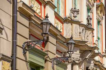 the facade of a historic tenement house decorated with rich architectural details. Attention is drawn to the decorative wall lamps with lanterns, carved decorative elements and colorful details of the