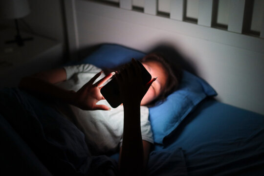 Young woman using smartphone in bed at night
