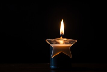 Glowing Candle in Star Shaped Holder with Warm Flame on Dark Table Against Black Backdrop Creates an Atmospheric and Peaceful Mood with a Single Flame and Soft Shadows