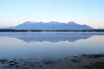 Fototapeta premium Misty lake reflecting mountains at dawn