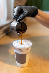 The barista pours coffee into a takeaway cup. Make a latte with ice in a cafe. Summer, relaxation, cooling drinks