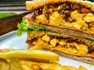 Close-up vertical shot of a sandwich and fries on a blue rimmed plate, capturing the textures and layers of the ingredients in great detail.