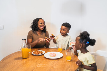 African smiling mother and children sharing a cheerful breakfast of pastries and juice at home, enjoying quality family time