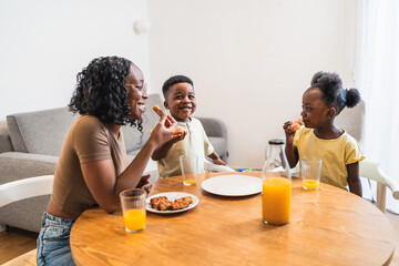 Cheerful african mother and children sharing a pleasant breakfast together at the dining table in their cozy home