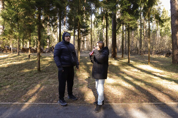 Two people stand in a pine forest clearing on a cool day, bundled in winter jackets and enjoying a quiet moment surrounded by nature, representing outdoor bonding, eco-tourism, or casual hiking themes