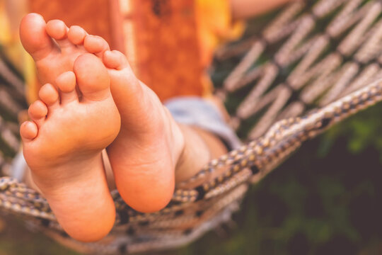 Young beautiful girl lies in a hammock and reads a book. Rest, summer vacation, leisure time concept. Selective focus on feets. Copy space for design.