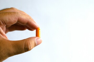 Hand holding an orange pill medicine on a white background