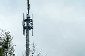 Communication tower stands tall against a cloudy sky in a rural area surrounded by trees