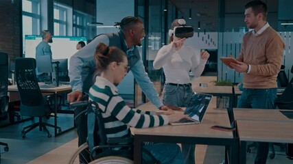 Disabled businesswoman in a wheelchair working in modern coworking office. Team around is using virtual reality goggles, collaborating with the latest technology in an open space startup creative - Powered by Adobe