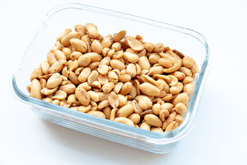 A close-up of a clear glass container filled with roasted peanuts. Healthy snack.