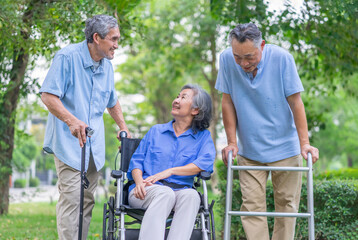 three of elderly friends with wheelchair,walker and cane enjoy talking together in nature park,aging society and health care concept