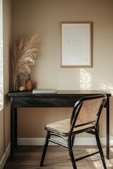 Simple, neutral workspace with a dark desk, woven chair, and pampas grass.  Framed art piece on the wall