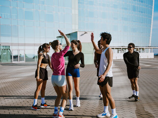 Fototapeta premium Side view of a happy Black 30-year-old man giving a high five to a dark-haired European adult woman while other multi-ethnic friends are talking on the street.