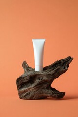 A simple, white tube of product sits atop a piece of driftwood against an orange backdrop. The wood grain is visible, showcasing texture and natural beauty.  The product tube is clean and minimalist