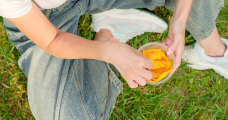 Close-up of a girl picking dried mango from a container in the park.