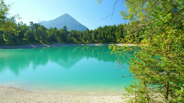 Alpine lake Urisee with still turquoise waters and forested surroundings in Reutte Tirol, relaxing nature scenery in the mountains