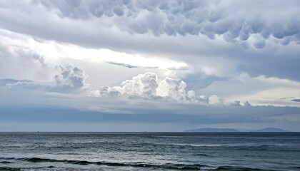 Obraz premium Dramatic seascape featuring turbulent, mammatus clouds over a tranquil ocean. Ideal for concepts of weather, natures power, or emotional landscapes.