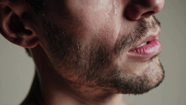 Close-up of emotional man crying &mdash; tears on cheek and lips trembling in silence, concept of vulnerability and mental health