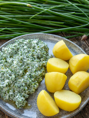 Homemade Greek Yogurt Chive dip with cooked potatoes on a plate. Chive steams, some with flower buds in the background. Rustic wooden table. 