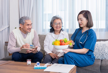 home health care nurse in uniform explaining nutritional value of fruits,vitamins and dietary fiber to senior couple,old man writing on notebook