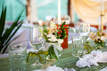 Wedding table setting with candles, flowers and glassware on green textile, romantic outdoor reception decor with natural elements, minimalist boho style arrangement for event celebration