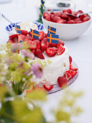 A close up of a table set with a cake of strawberries and whipped cream and a bowl of straberries...