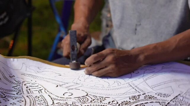 Close-up hand of the craftsman is meticulously crafting traditional shadow puppets using tools and intricate techniques in a workshop.