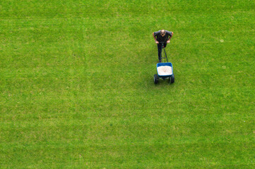 Groundsman spreads fertilizer for grass on a football pitch