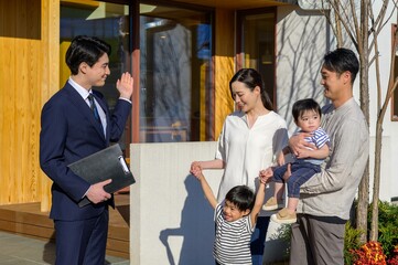 営業マンが若い夫婦と子どもに玄関先で挨拶している住宅訪問シーン