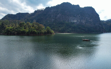 Fototapeta premium Aerial view of a long tail boat sailing in the river with mountain views