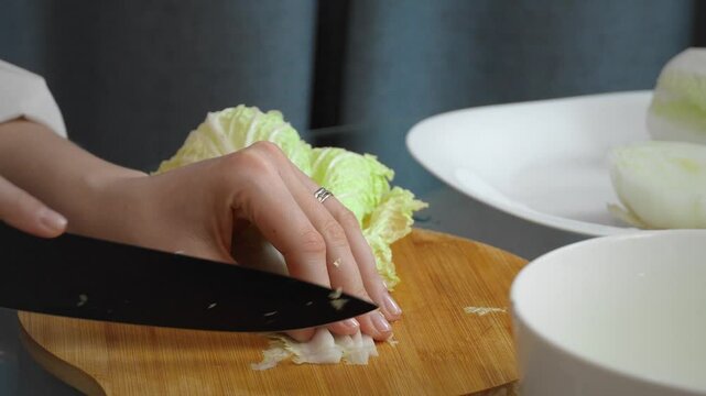 Professional female chef carefully slices fresh Chinese nappa cabbage on a wooden cutting board, prepares clean, bright ingredients for a nutritious meal in a modern kitchen setting
