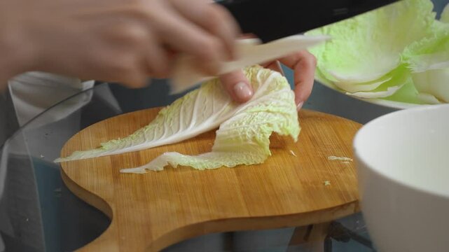 Professional female chef carefully slices fresh Chinese nappa cabbage on a wooden cutting board, prepares clean, bright ingredients for a nutritious meal in a modern kitchen setting